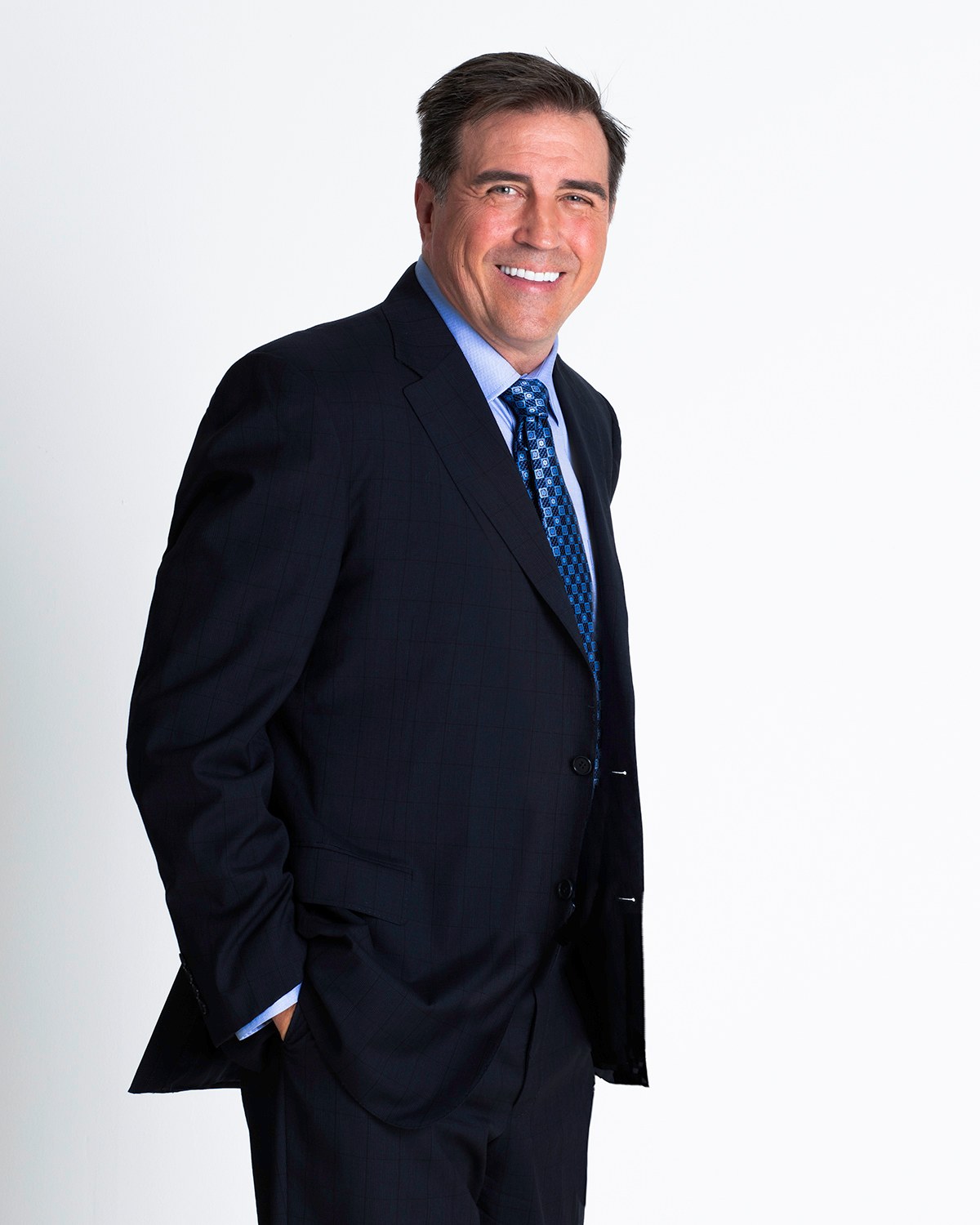 Man in a navy suit and patterned tie standing with hands in his pockets, white backdrop, photographed by Annie Watson in her Naples studio