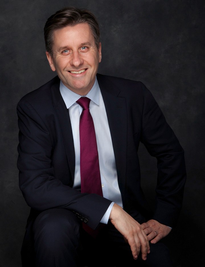 Man in a dark suit and red tie, seated and smiling, dark gray backdrop, photographed by Annie Watson in her Naples studio